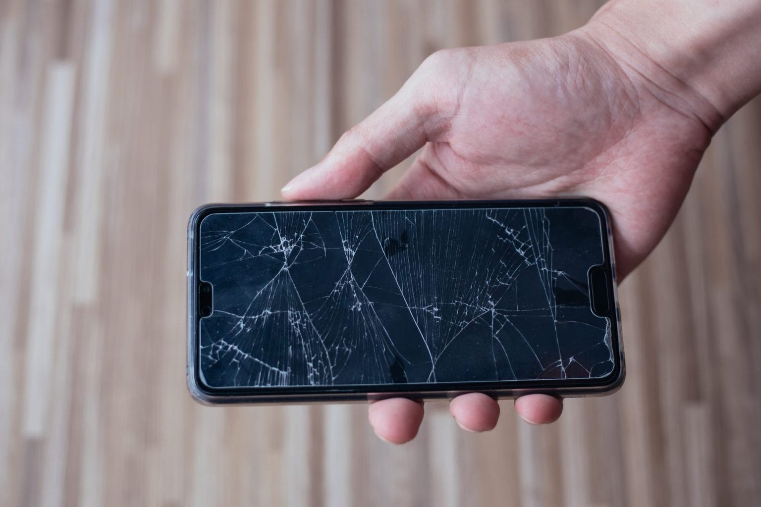 Close-up of human hand holding a broken and damaged glass of mobile phone from accident.
